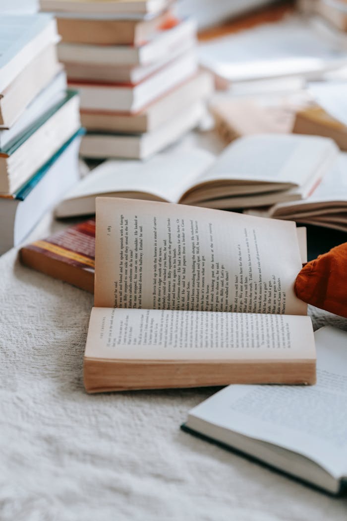 Collection of closed and opened books with text placed on white fabric in light room at home with various literature
